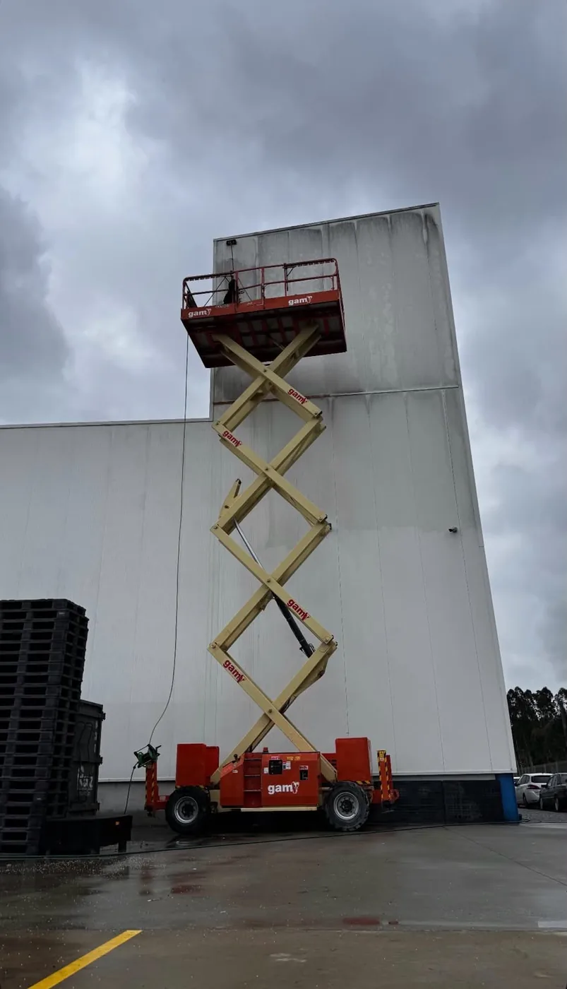 Plataforma elevatória de tesoura estendida junto a uma fachada industrial de grande altura