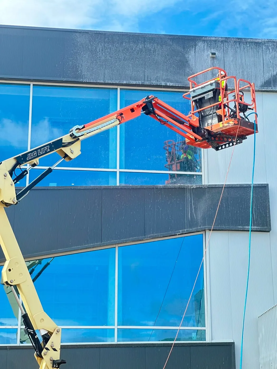 Trabalhador em plataforma elevatória articulada a limpar a fachada envidraçada de um edifício