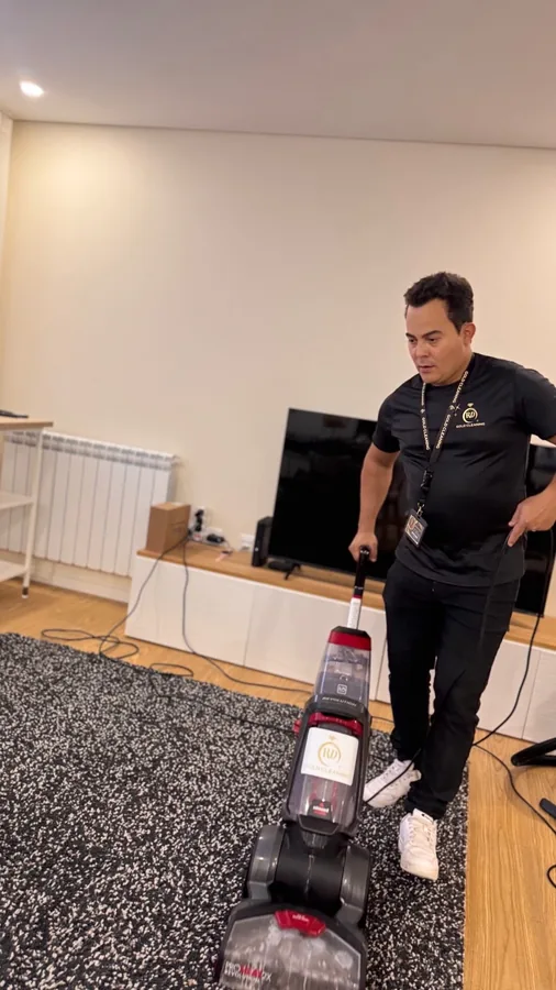 Profissional da Gold Cleaning a lavar uma carpete com máquina de limpeza profunda numa sala