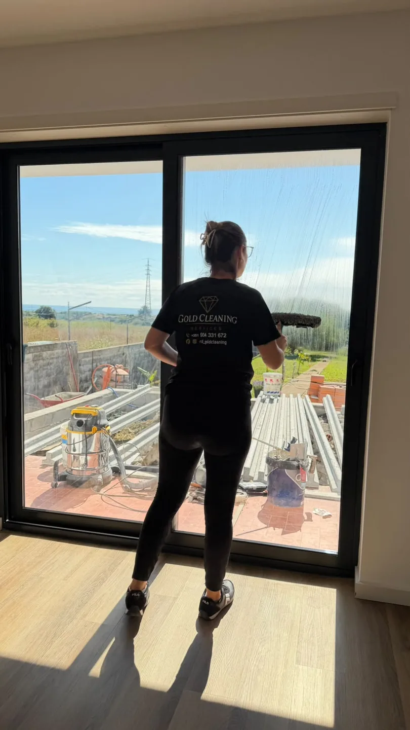 Profissional da Gold Cleaning, com t-shirt da marca, a lavar um vão envidraçado com vista para o exterior