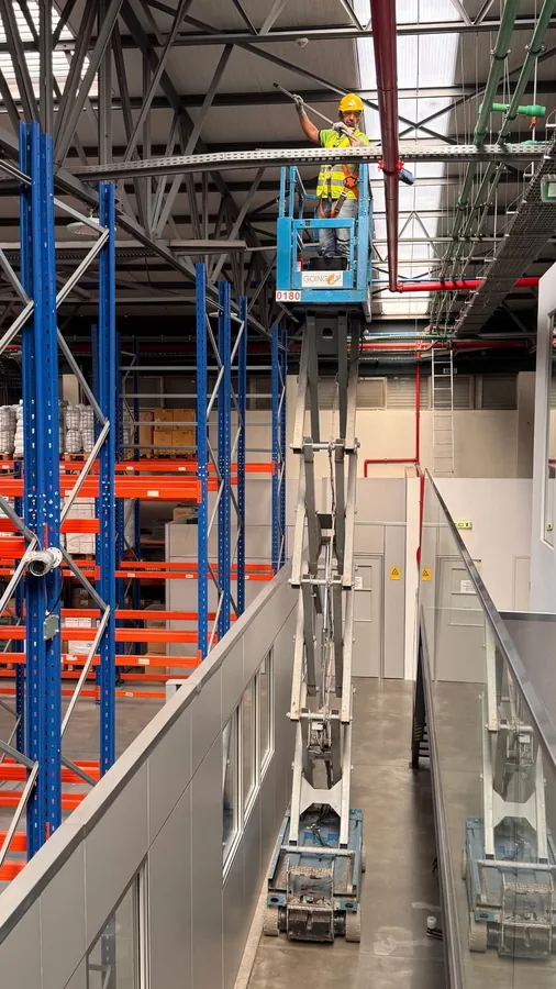 Profissional em plataforma elevatória a limpar a estrutura e as prateleiras de um armazém industrial