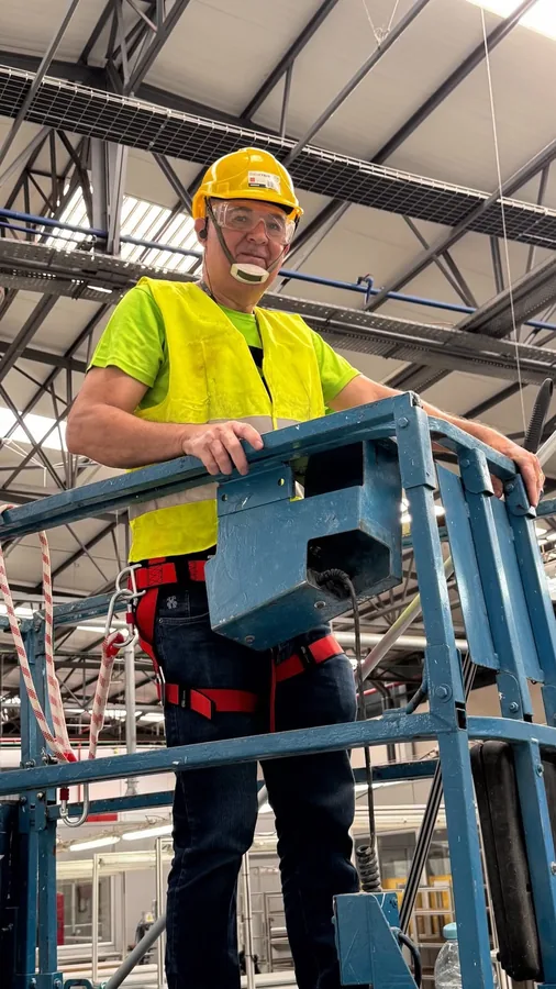 Profissional equipado com capacete e colete numa plataforma, em limpeza industrial