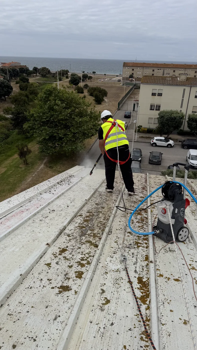 Trabalhador com arnês e capacete a lavar um telhado com máquina de alta pressão
